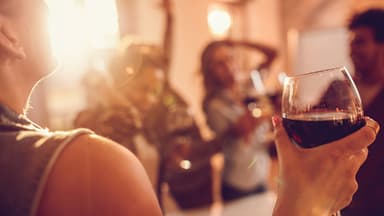 Frau trinkt ein Glas Rotwein. Gegen einen Kater helfen diese Tipps. 