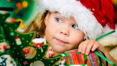 Kleines Mädchen mit Weihnachtsmütze lugt hinter dem Tannenbaum hervor