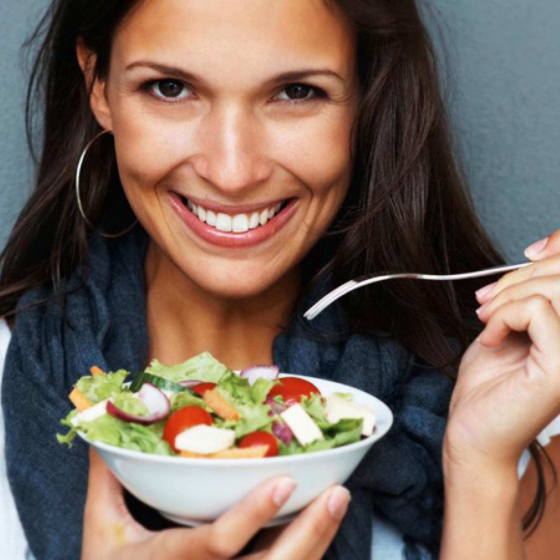 Dunkelhaarige, lachende Frau isst Salat