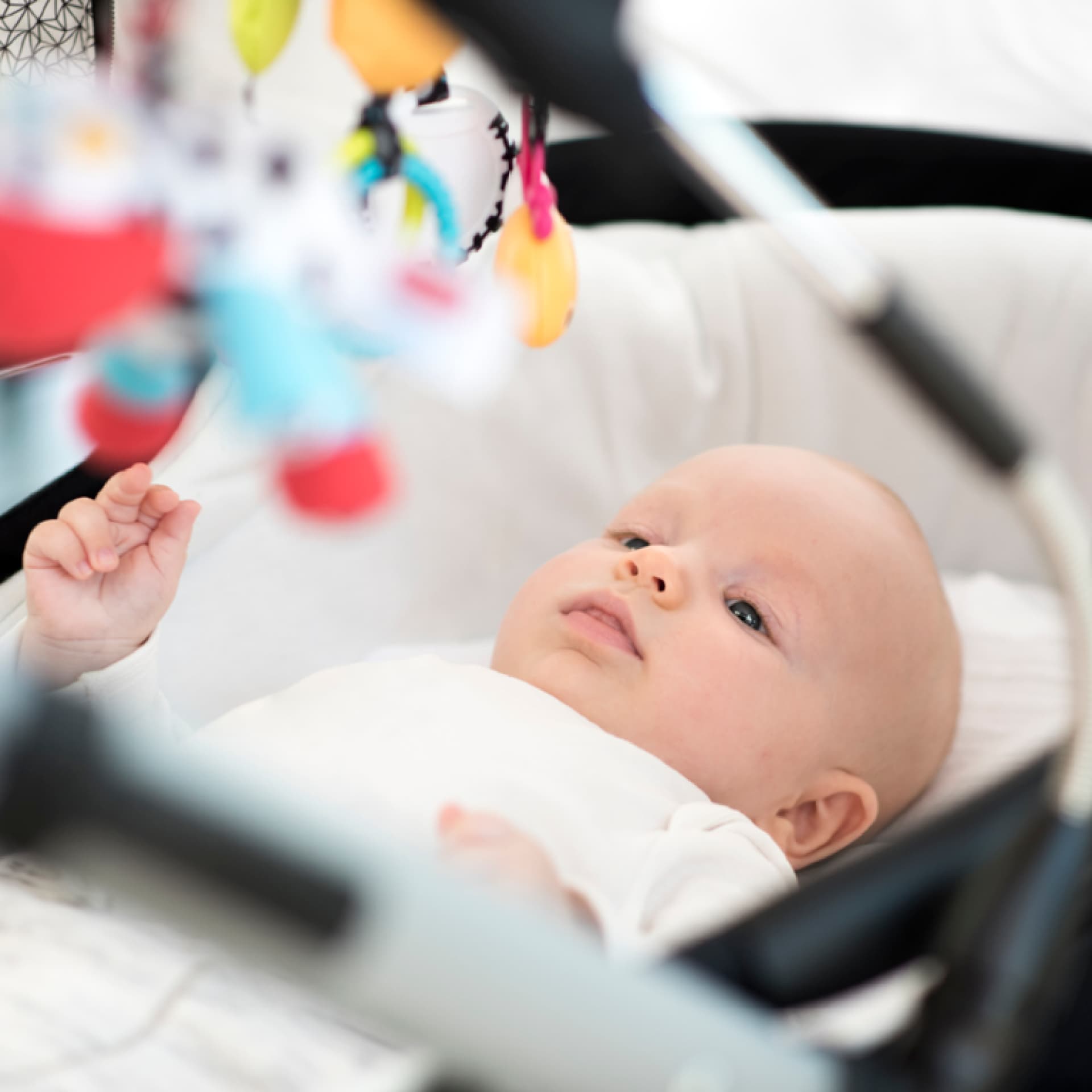 Baby liegt im Kinderwagen und schaut seine Kinderwagenkette