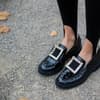 Frau trägt schwarze Loafer mit großer Schnalle.