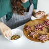Frau verziert weihnachtliche Plätzchen mit Zuckerguss und bunten Streuseln.