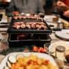 Ein Raclette-Gerät steht auf einer festlich gedeckten Tafel.