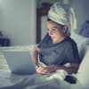 Frau am Laptop im Bett will mit nassen Haaren schlafen gehen