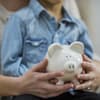 Sparschwein in der Hand von einer Frau mit einem Kind auf dem Schoß