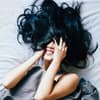 Frau liegt im Bett und hat ihre Haare im Gesicht