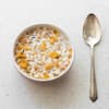 Cornflakes mit Milch in einer Schüssel mit einem Löffel daneben