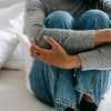 Frau sitzt auf Bett mit angezogenen Knien.