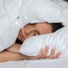 Frau liegt im Bett mit der Decke über dem Kopf