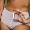 Frau hält einen Tampon vor ihrem Unterleib in der Hand.
