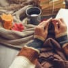 Frau strickt und hat ein Strickbuch parat