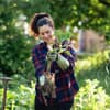 Eine Frau mit Gartenhandschuhen hält Unkraut samt Wurzel in der Hand