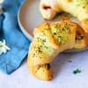 Pizzateig-Croissants mit Käse-Gewürz-Topping neben einem Teller angerichtet 