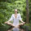Eine Frau macht den Yoga Lotus-Sitz in einem grünen Wald