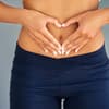 Eine Frau formt mit ihren Händen ein Herz auf dem Bauch Gibt es Bakterien, die dick machen?