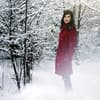 Frau steht im verschneiten Wald mit rotem Mantel - Tipps für das richtige Winteroutfit