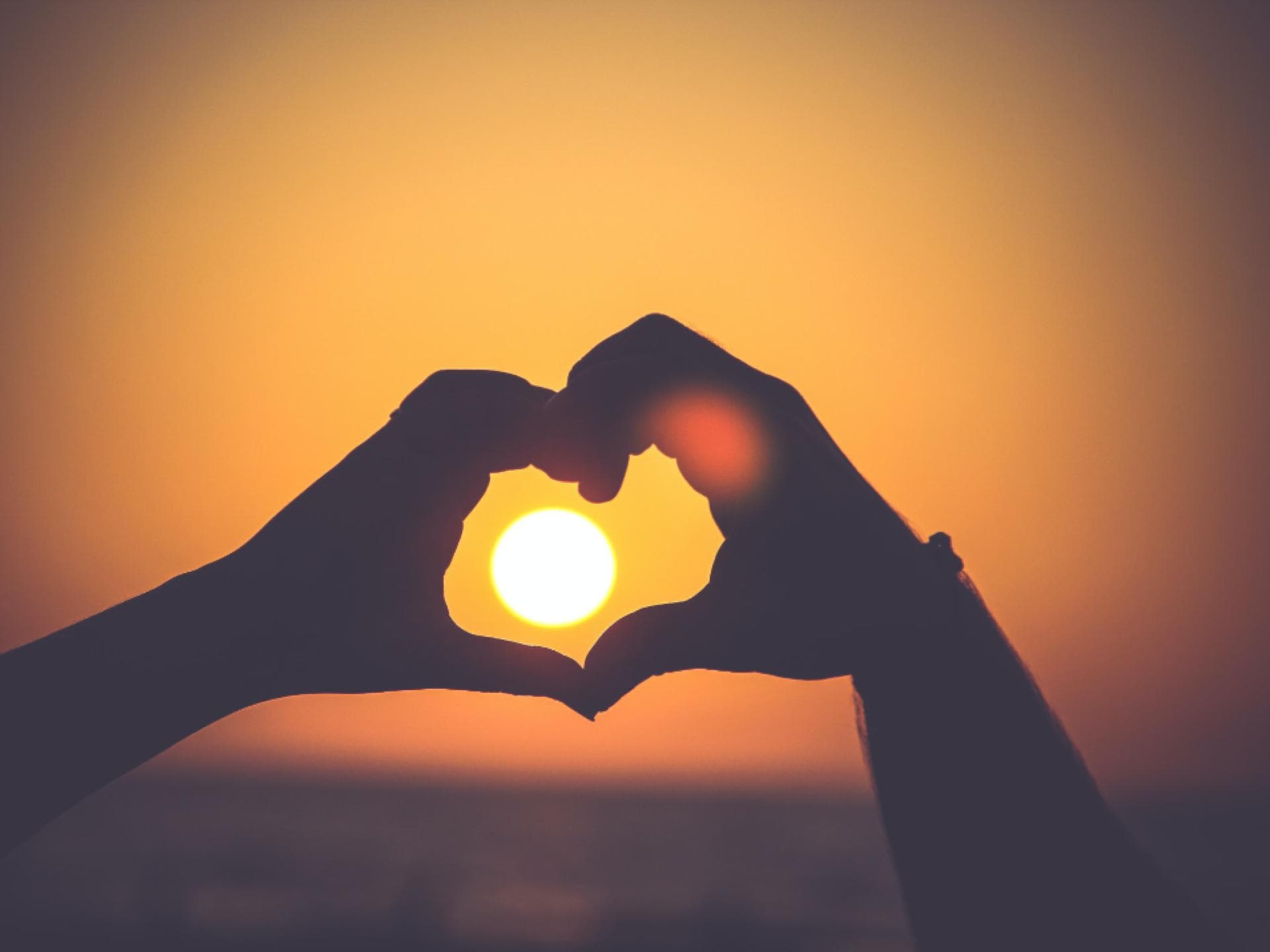 Hände formen ein Herz bei Sonnenuntergang