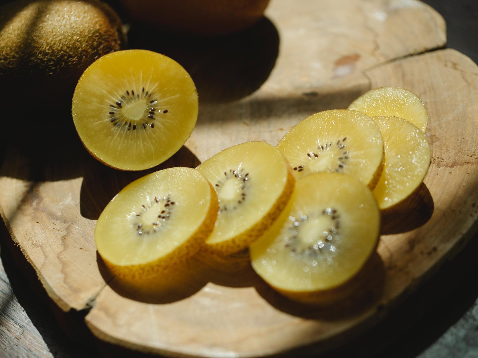 Eine aufgeschnittene, gelbe Kiwi auf einem Holzbrett.