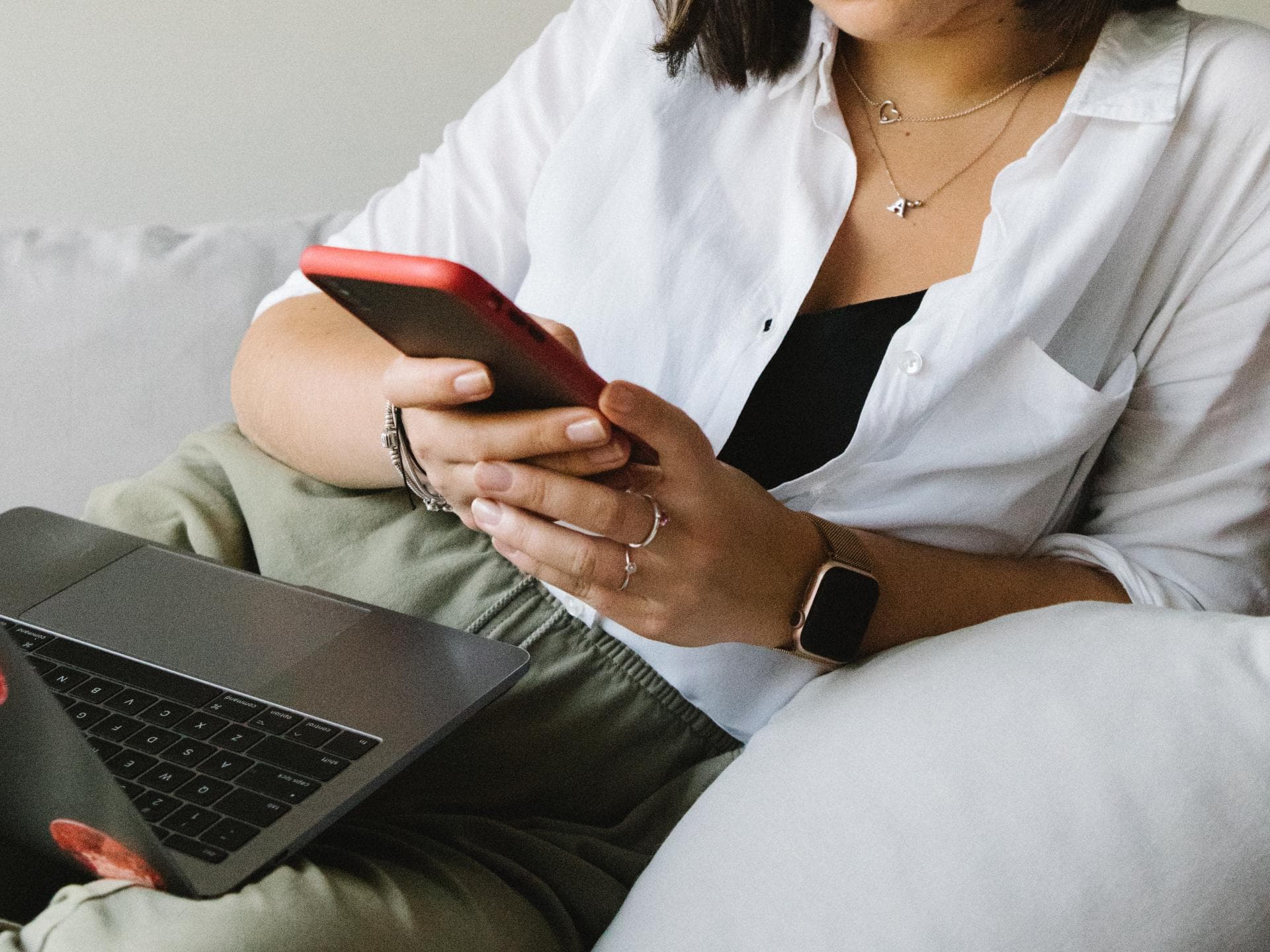 Eine Frau mit Laptop auf dem Schoß checkt ihr Smartphone. 