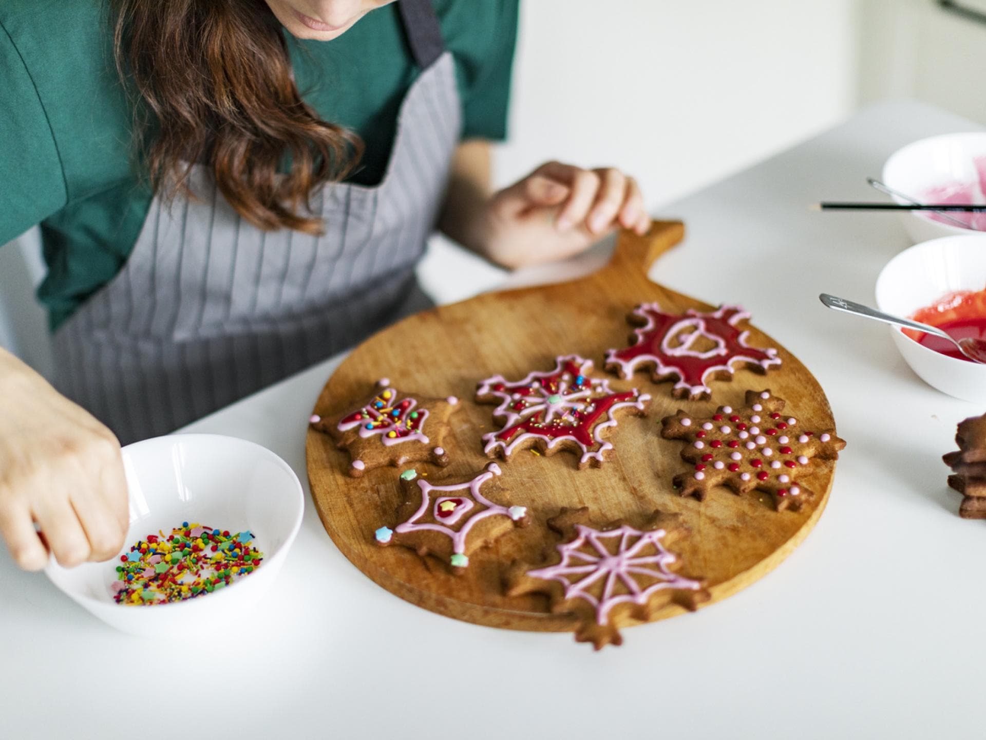 Frau verziert weihnachtliche Plätzchen mit Zuckerguss und bunten Streuseln.