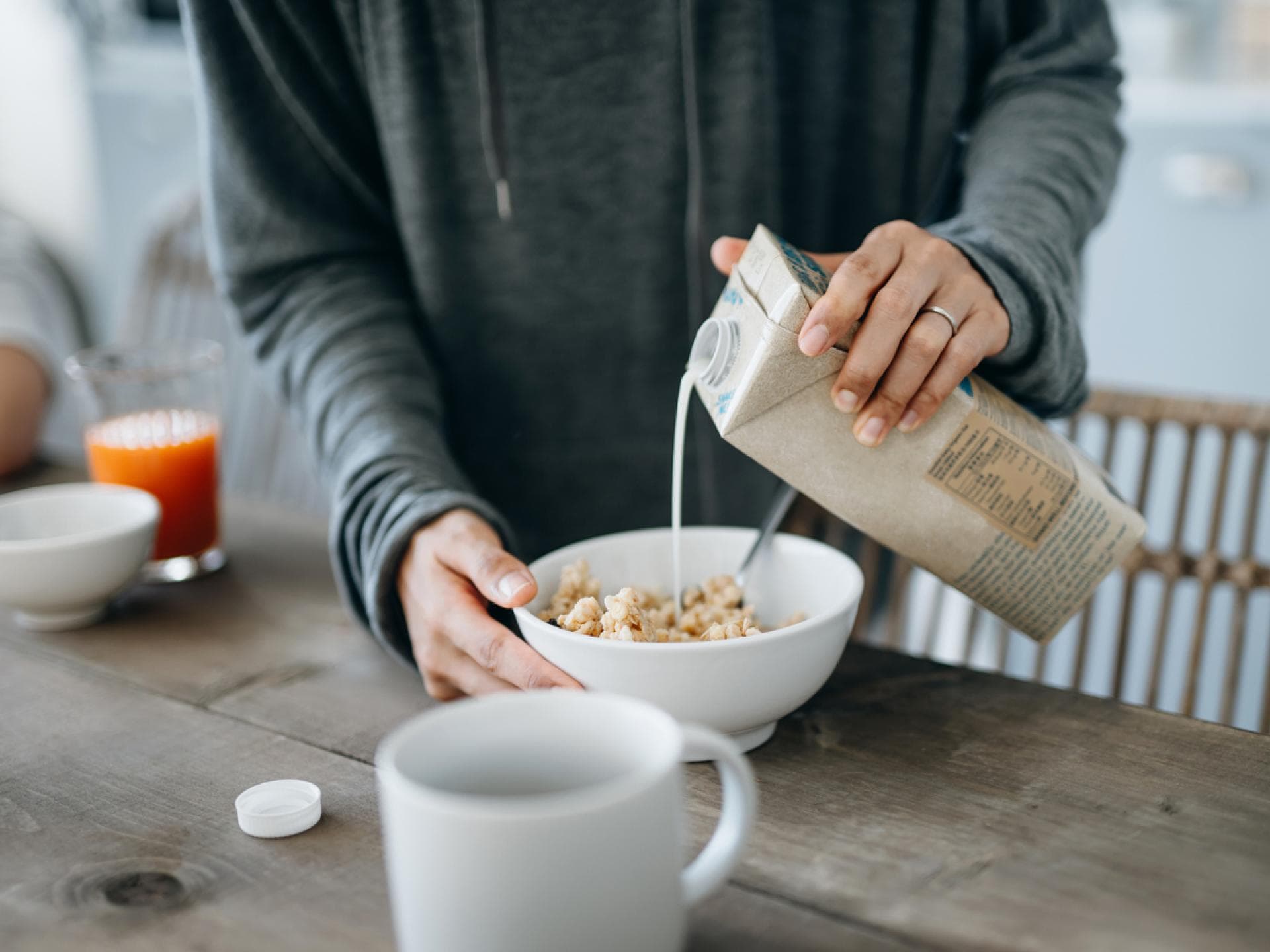 Frau gießt sich Hafermilch ins Müsli 