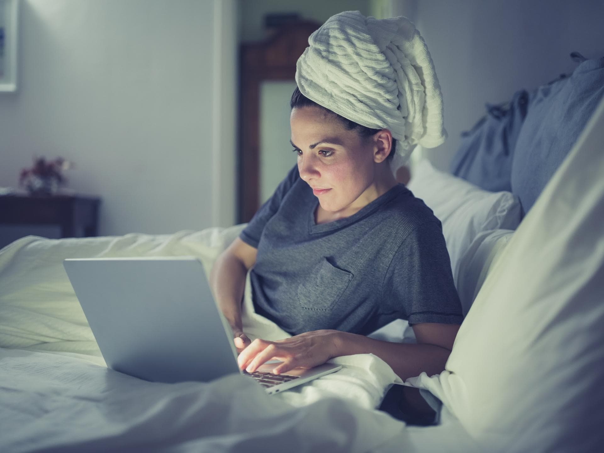 Frau am Laptop im Bett will mit nassen Haaren schlafen gehen