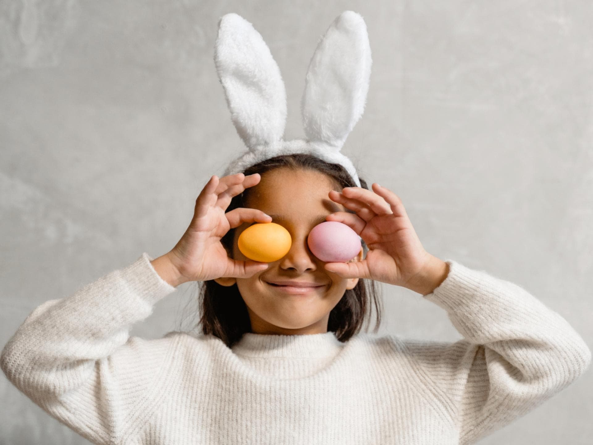 Kind mit Hasenohren hält sich zwei Ostereier vor die Augen Kind mit Hasenohren hält sich zwei Ostereier vor die Augen
