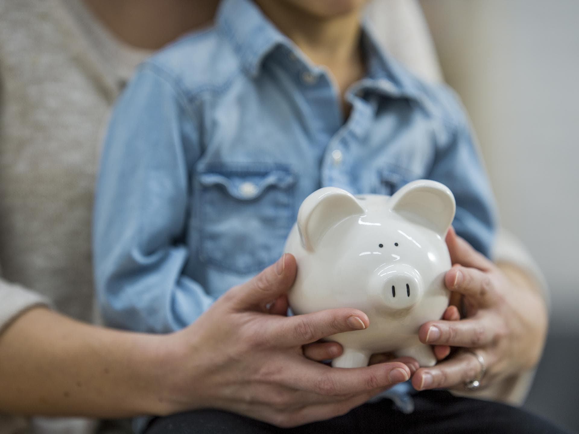 Sparschwein in der Hand von einer Frau mit einem Kind auf dem Schoß
