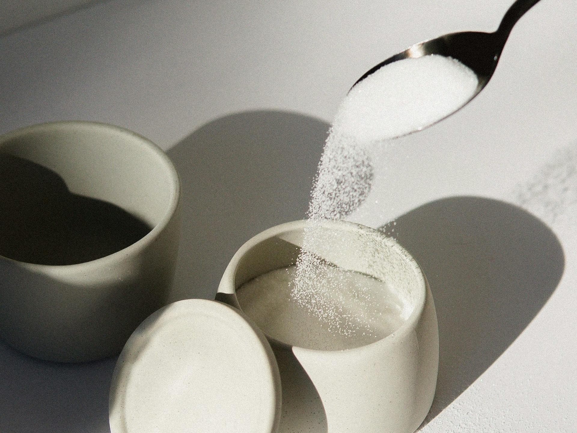 Zucker rieselt vom Löffel in eine Schale