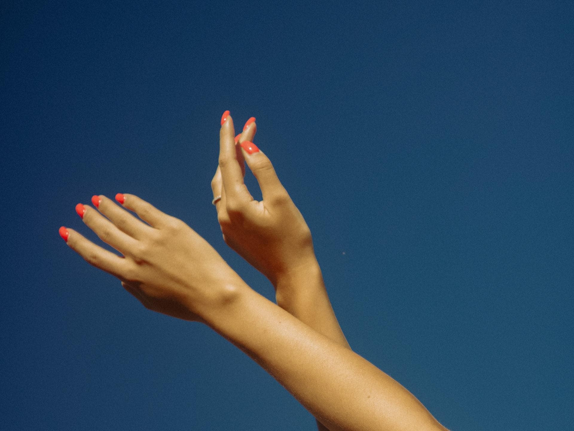 Hände im Himmel mit orangenen Nägeln