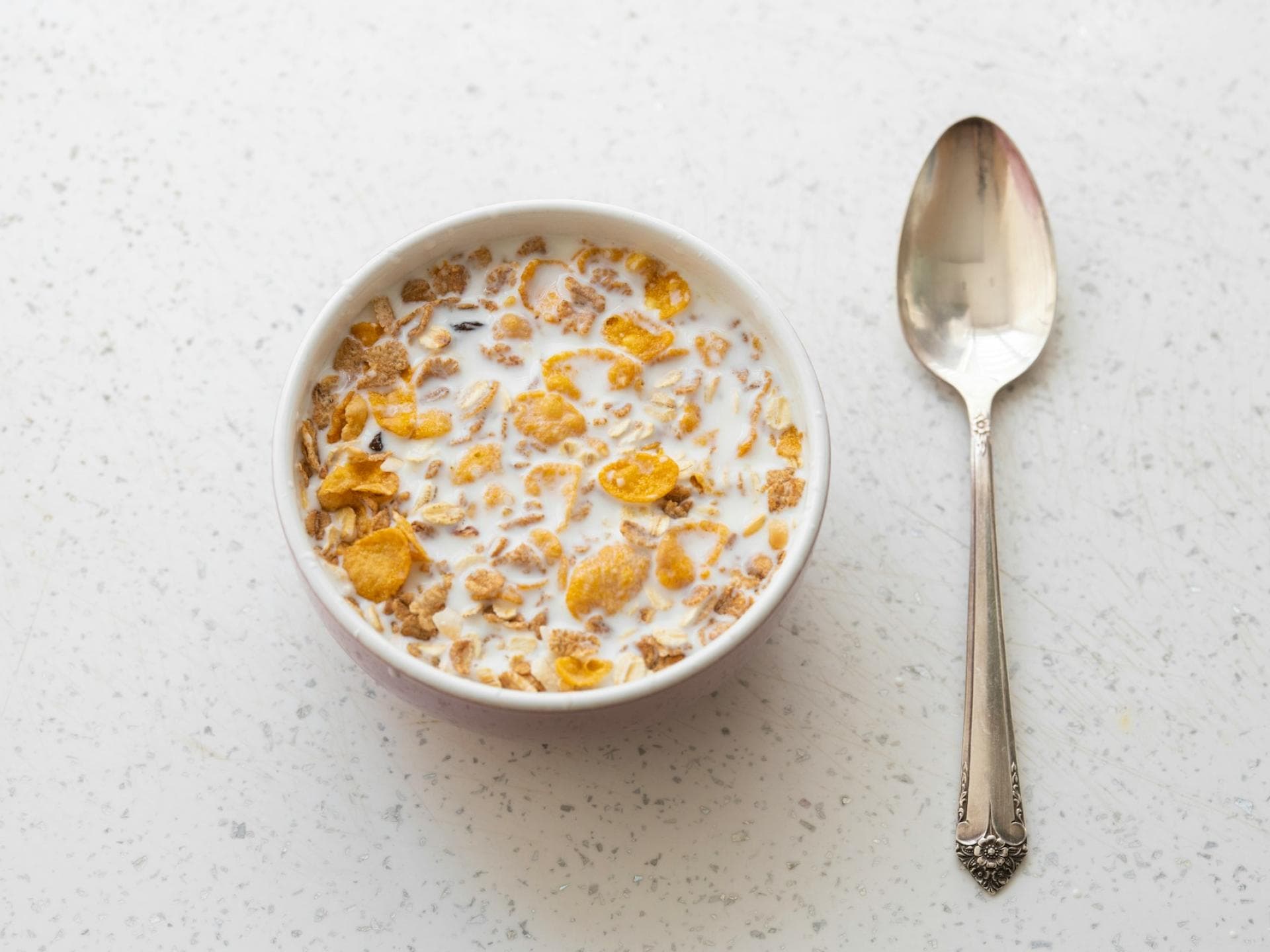 Cornflakes mit Milch in einer Schüssel mit einem Löffel daneben Cornflakes mit Milch in einer Schüssel mit einem Löffel daneben