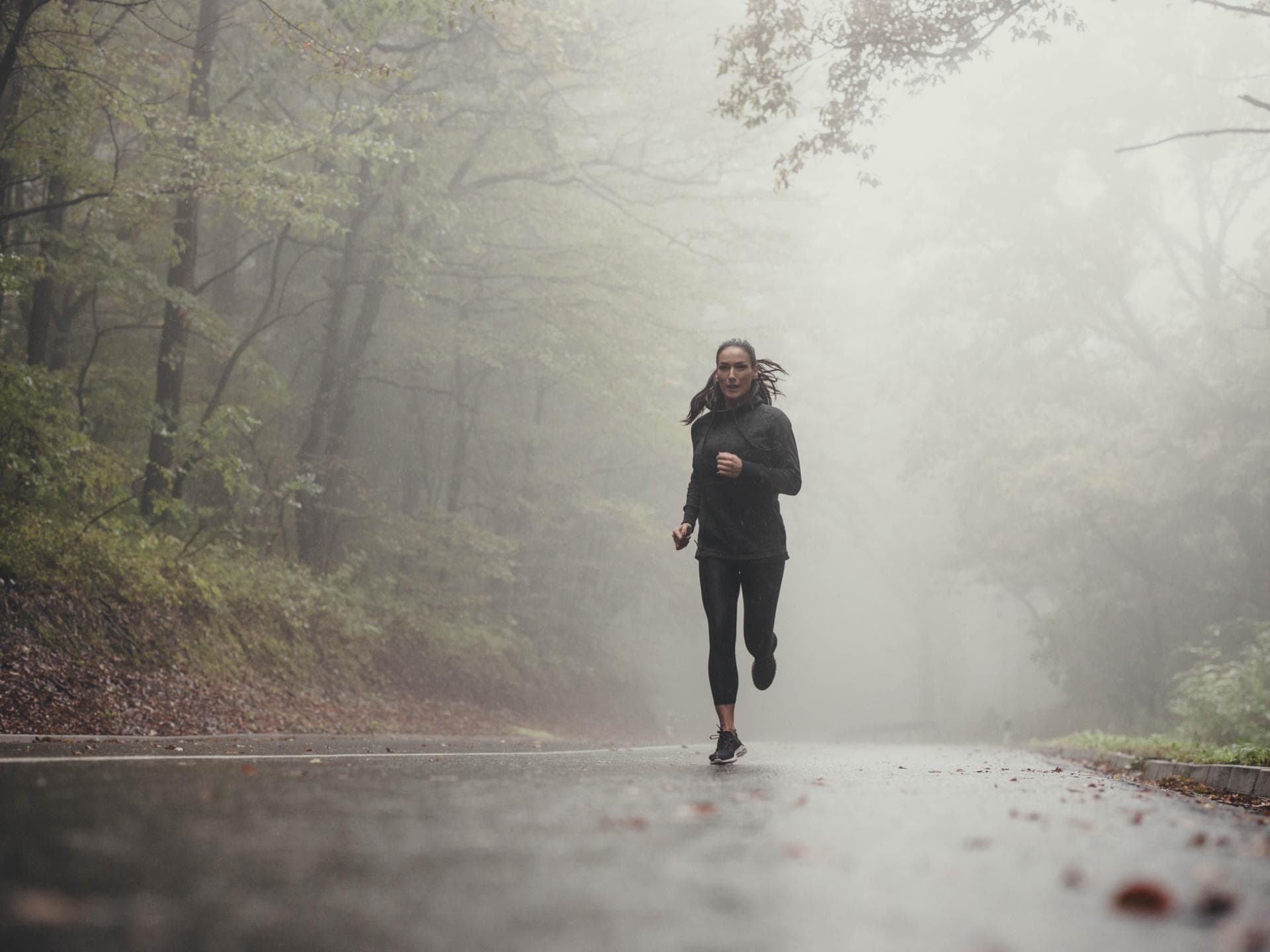 Frau beim Joggen bei Regen im Wald.