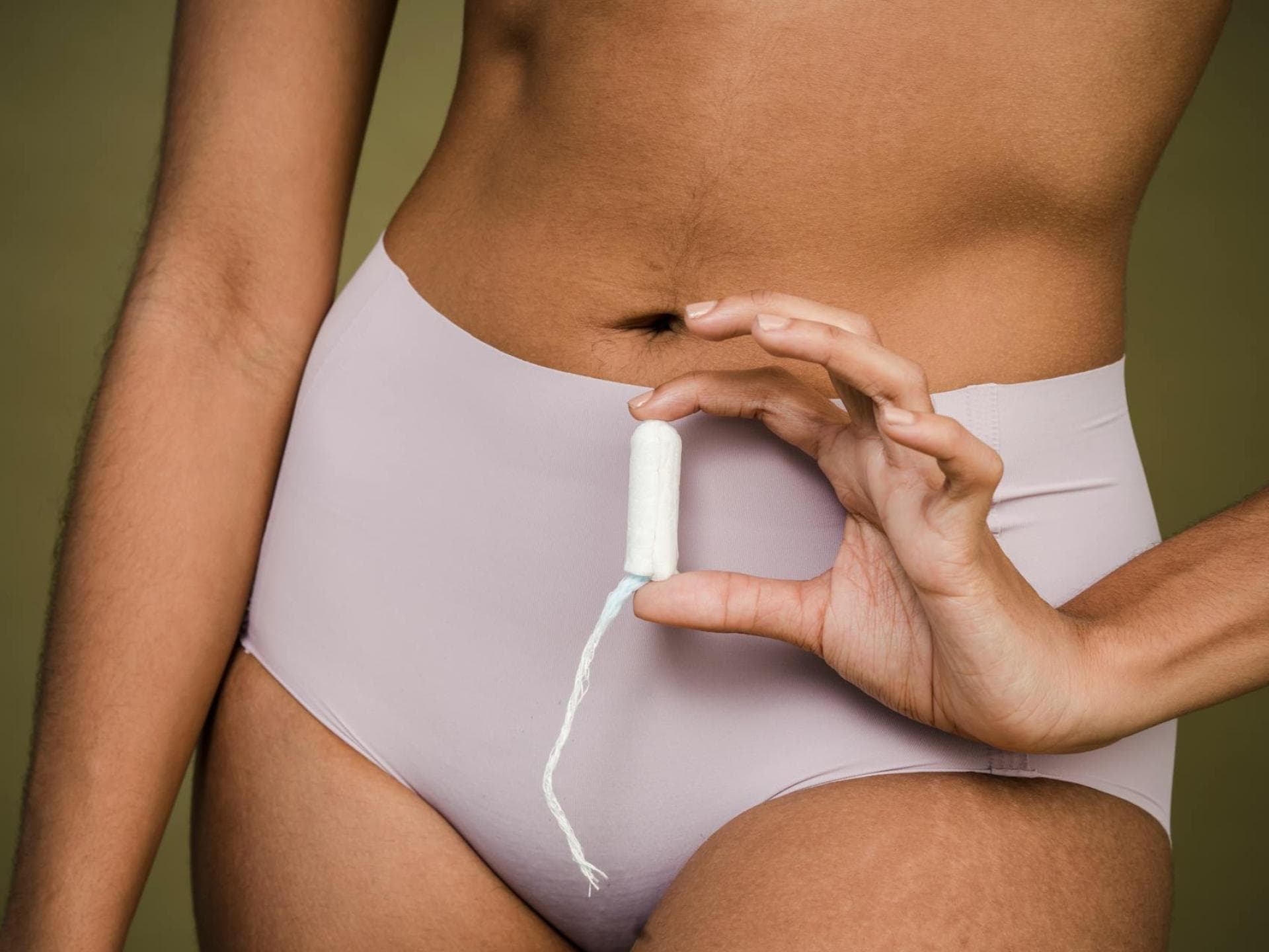 Frau hält einen Tampon vor ihrem Unterleib in der Hand.