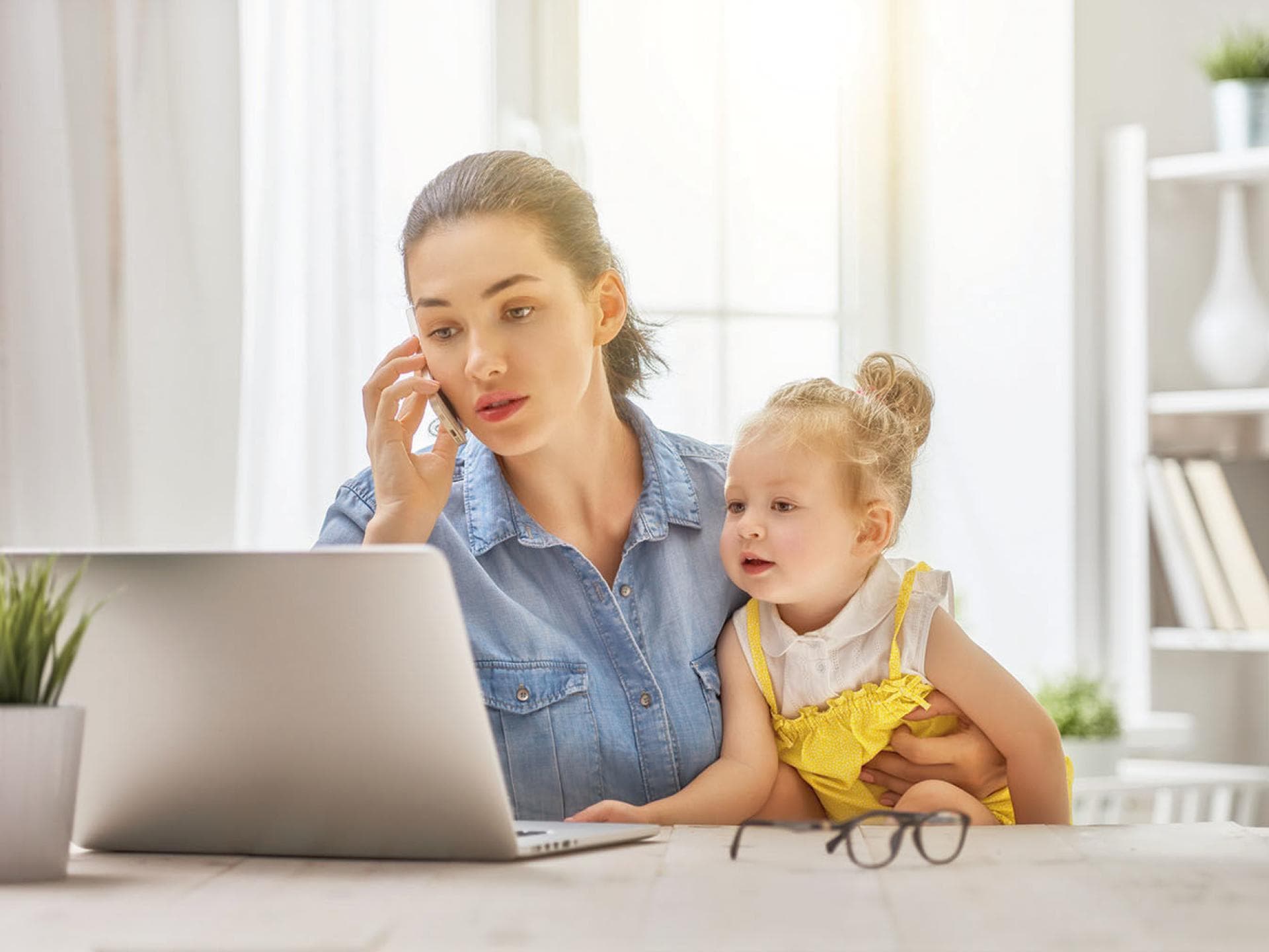 Eine junge Frau sitzt am Laptop mit einem Kleinkind