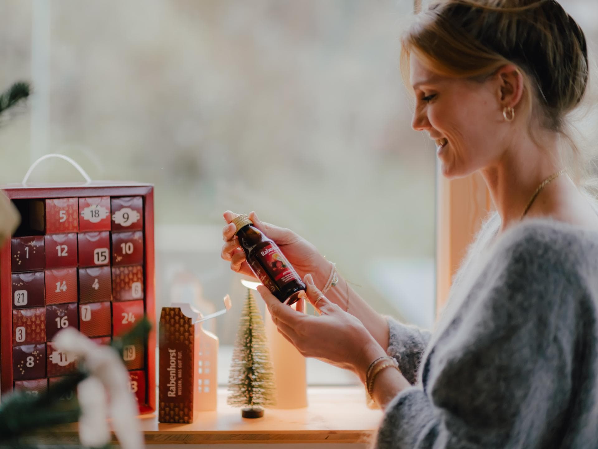 Rabenhorst-Adventskalender-Gewinnspiel Eine Frau hat das erste Türchen ihres Rabenhorst-Adventskalenders geöffnet und hält freudig strahlend einen Rabenhorst-Mini-Saft in der Hand