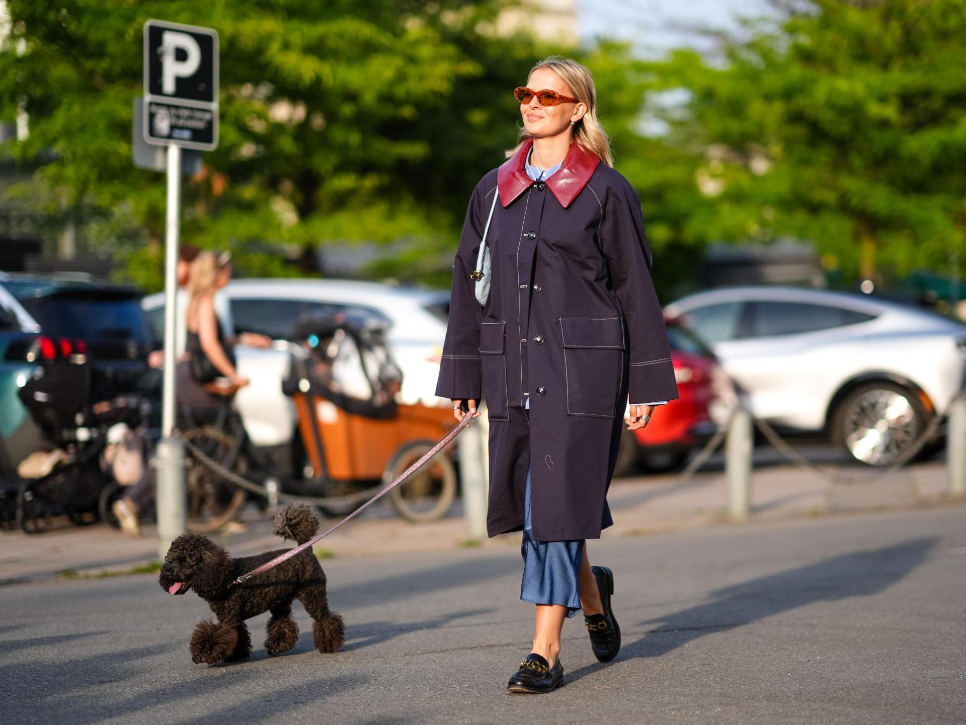 Eine blonde Frau, Mitte zwanzig, führt ihren Hund an einem sonnigen Frühlingstag in Kopenhagen durch die Straßen