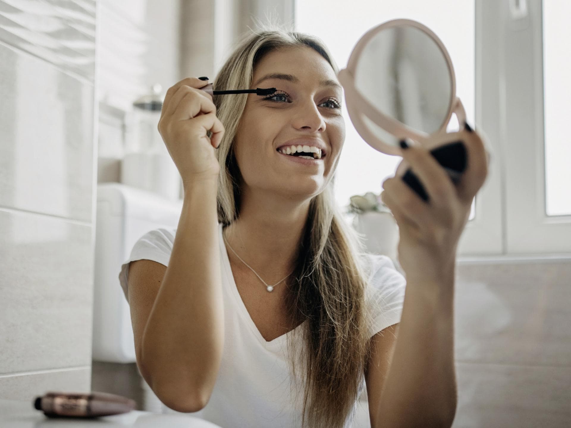 Blondine tuschte ihre Wimpern vor Handspiegel