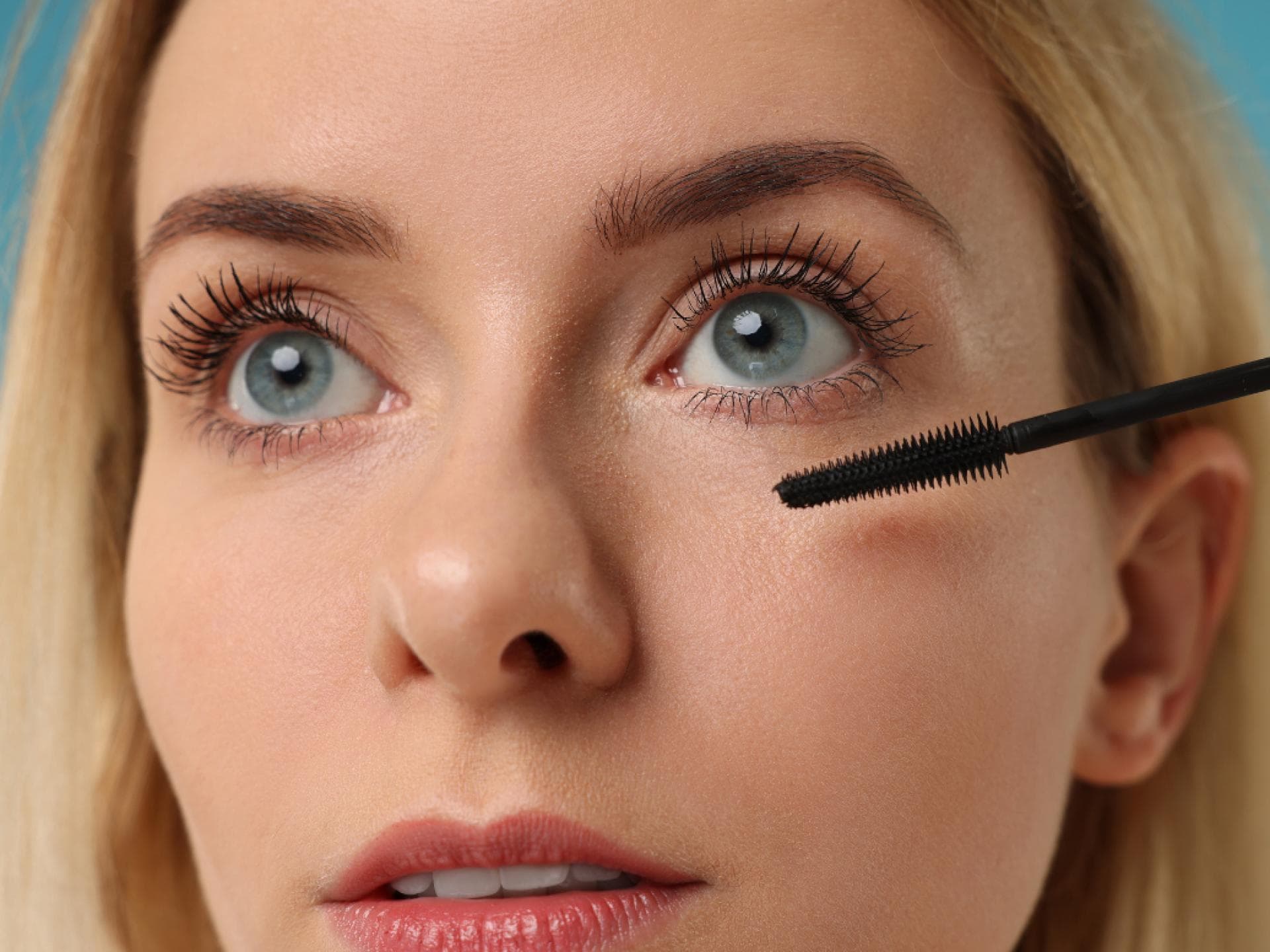 Blondine mit langen Wimpern trägt Mascara auf