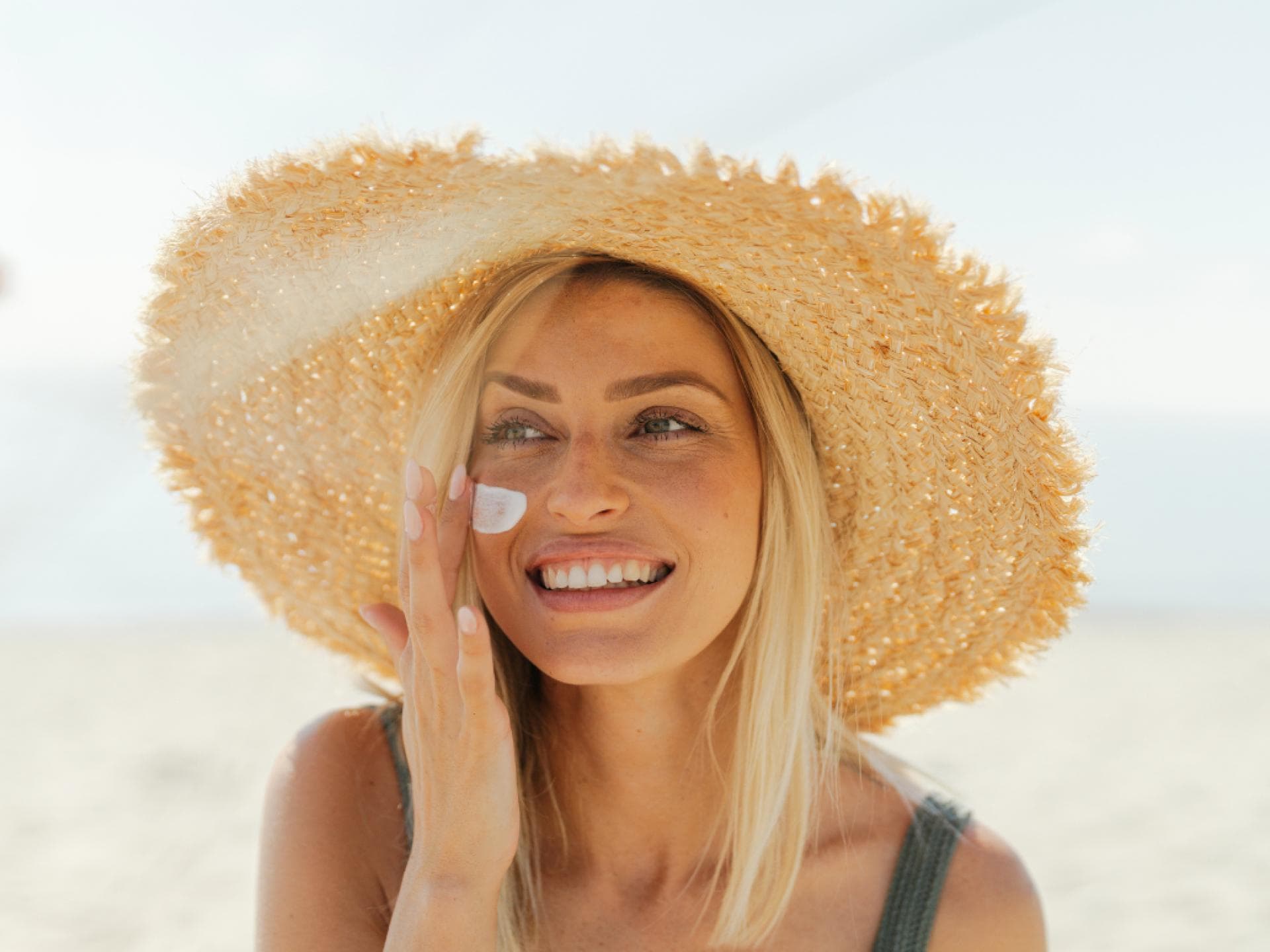 Frau mit Sonnenhut trägt Sonnencreme auf