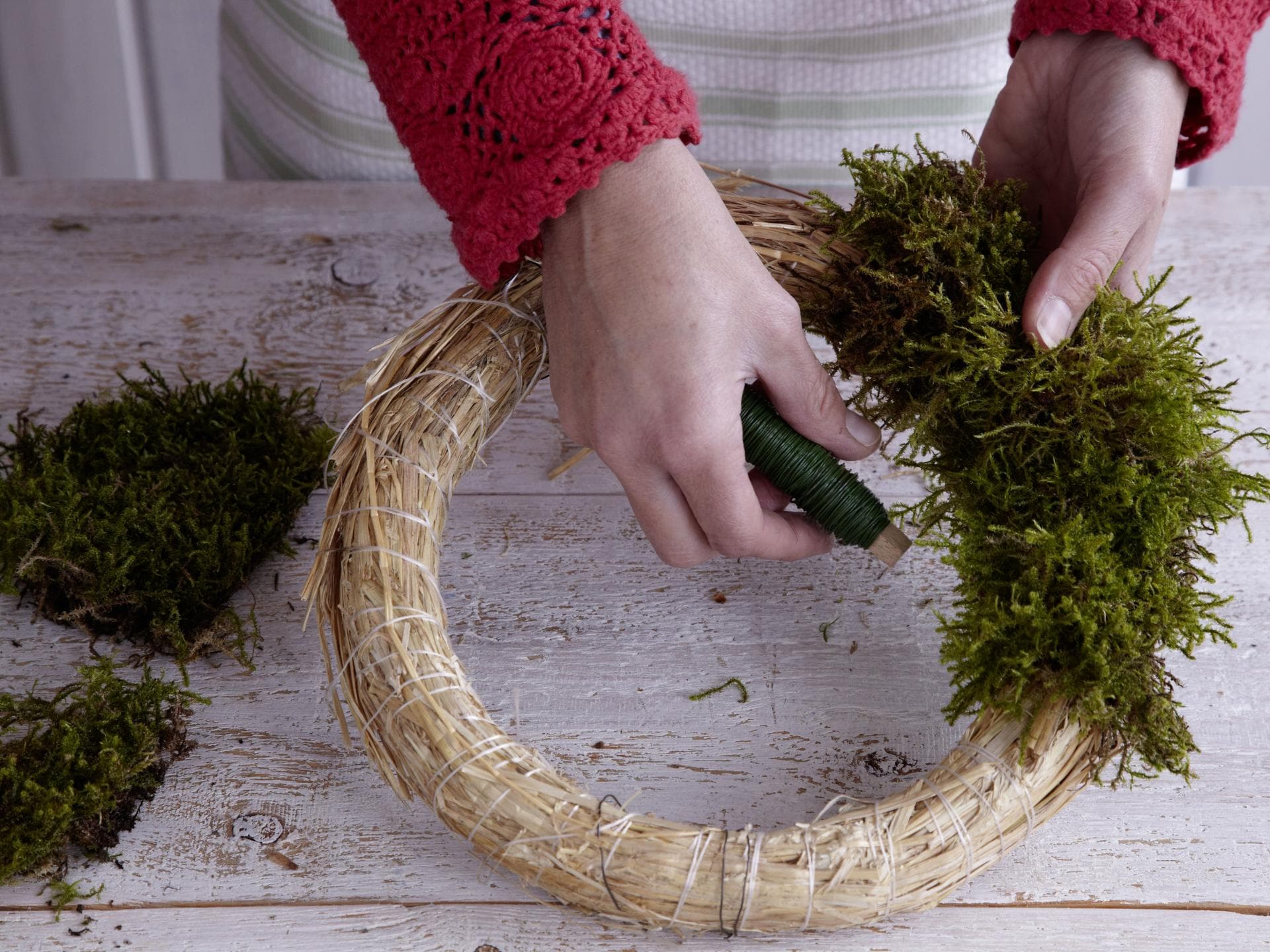 Frau wickelt Moos um Adventskranz