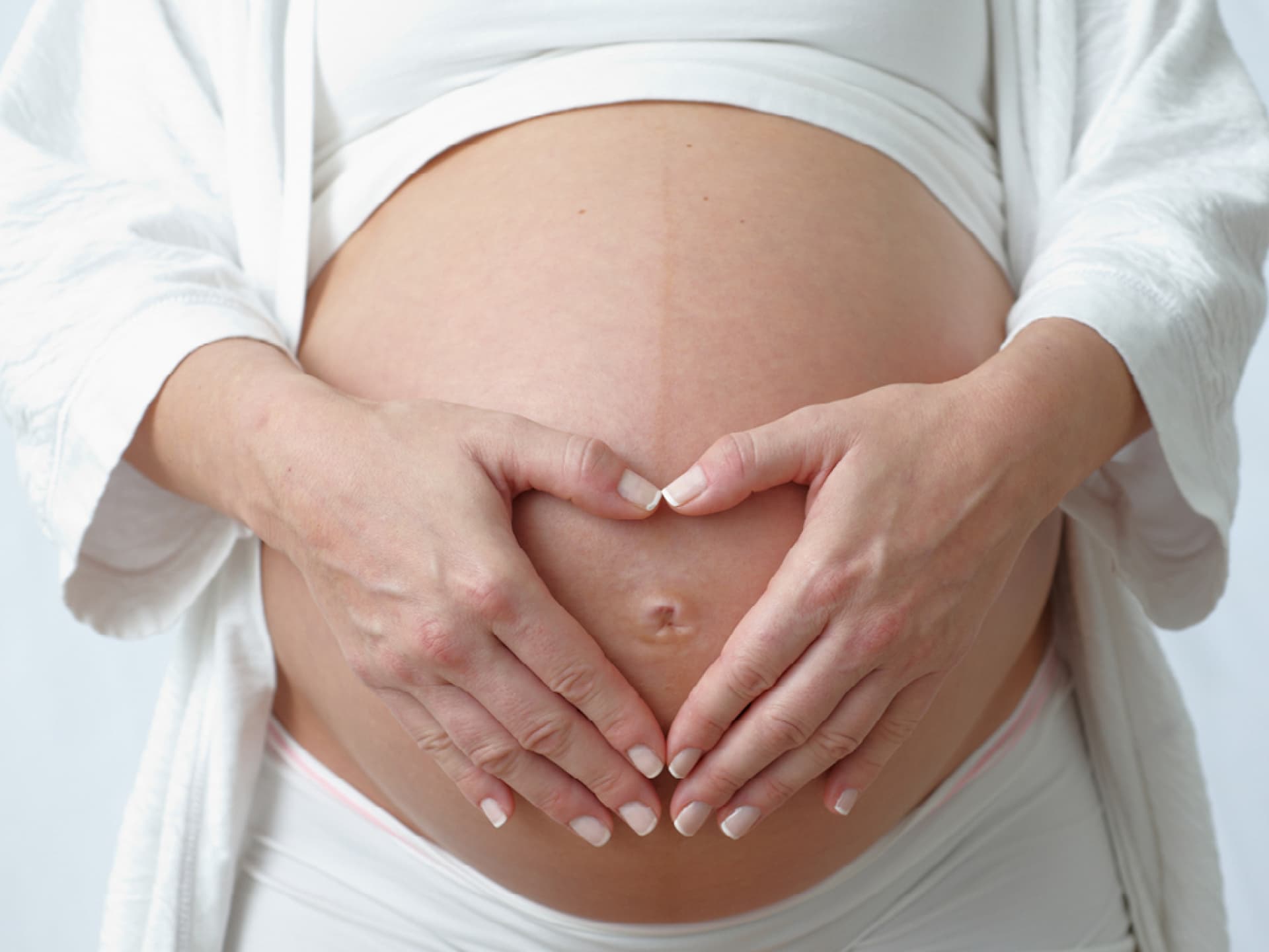 Eine hochschwangere Frau hält ihren Bauch. Sie erkennt erste Anzeichen einer bevorstehenden Geburt. 