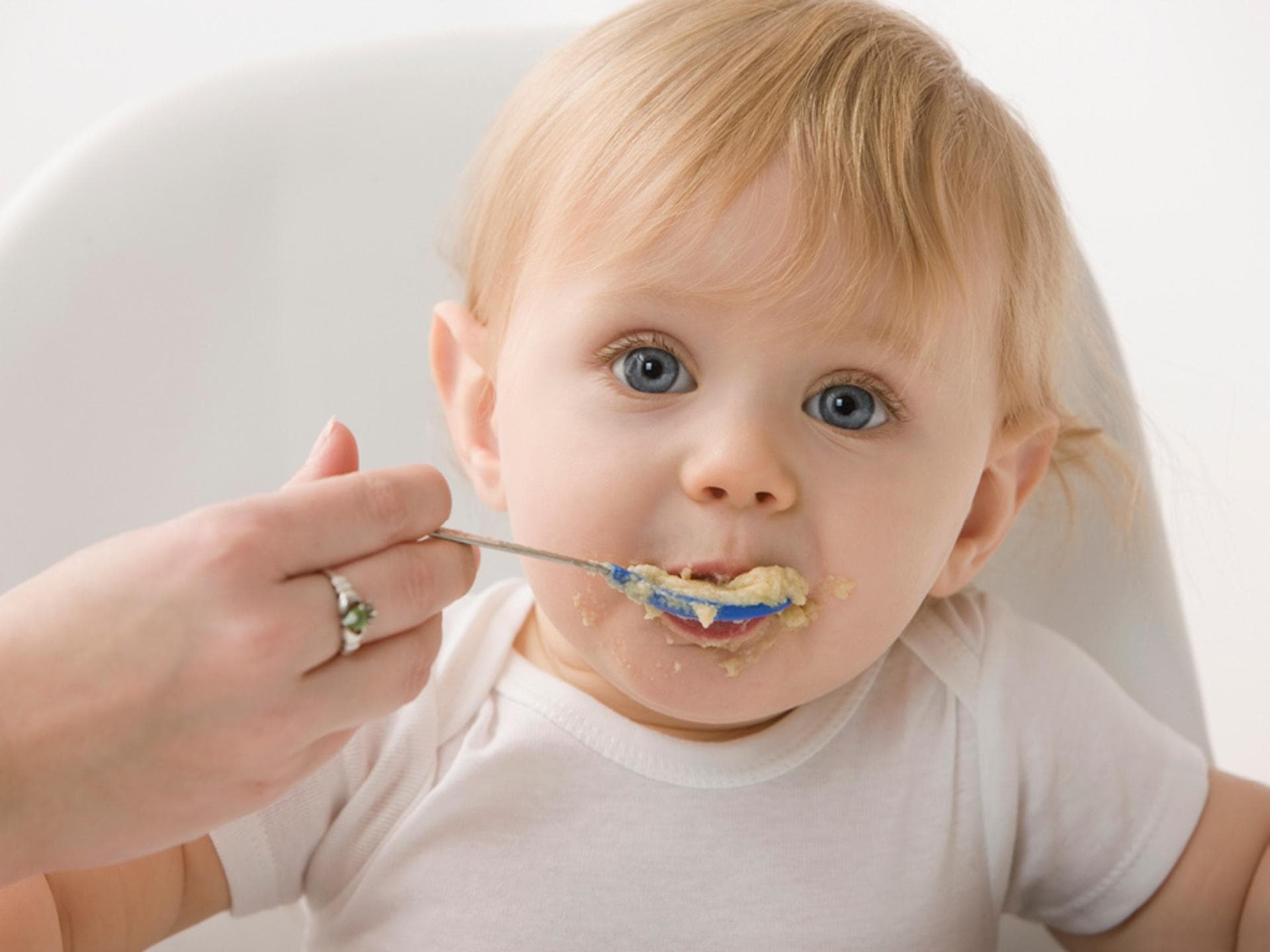 Getreidebrei für Babys NIedliches blondes Baby wird mit Brei gefüttert