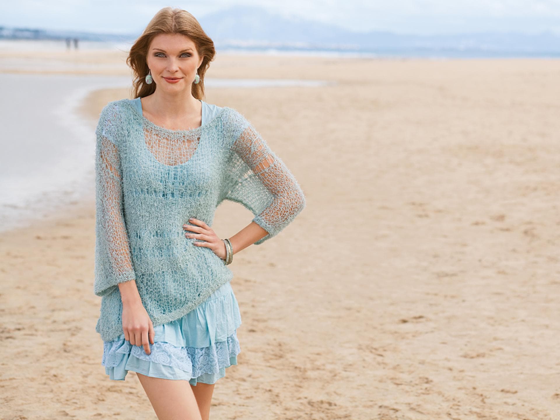 Frau mit transparentem Pulli in Mint steht am Strand