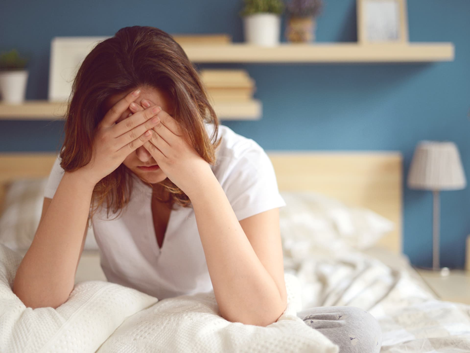 Frau sitzt im Bett und hat Kopfschmerzen Frau sitzt im Bett und hat Kopfschmerzen, doch diese Hausmittel helfen gegen Kater