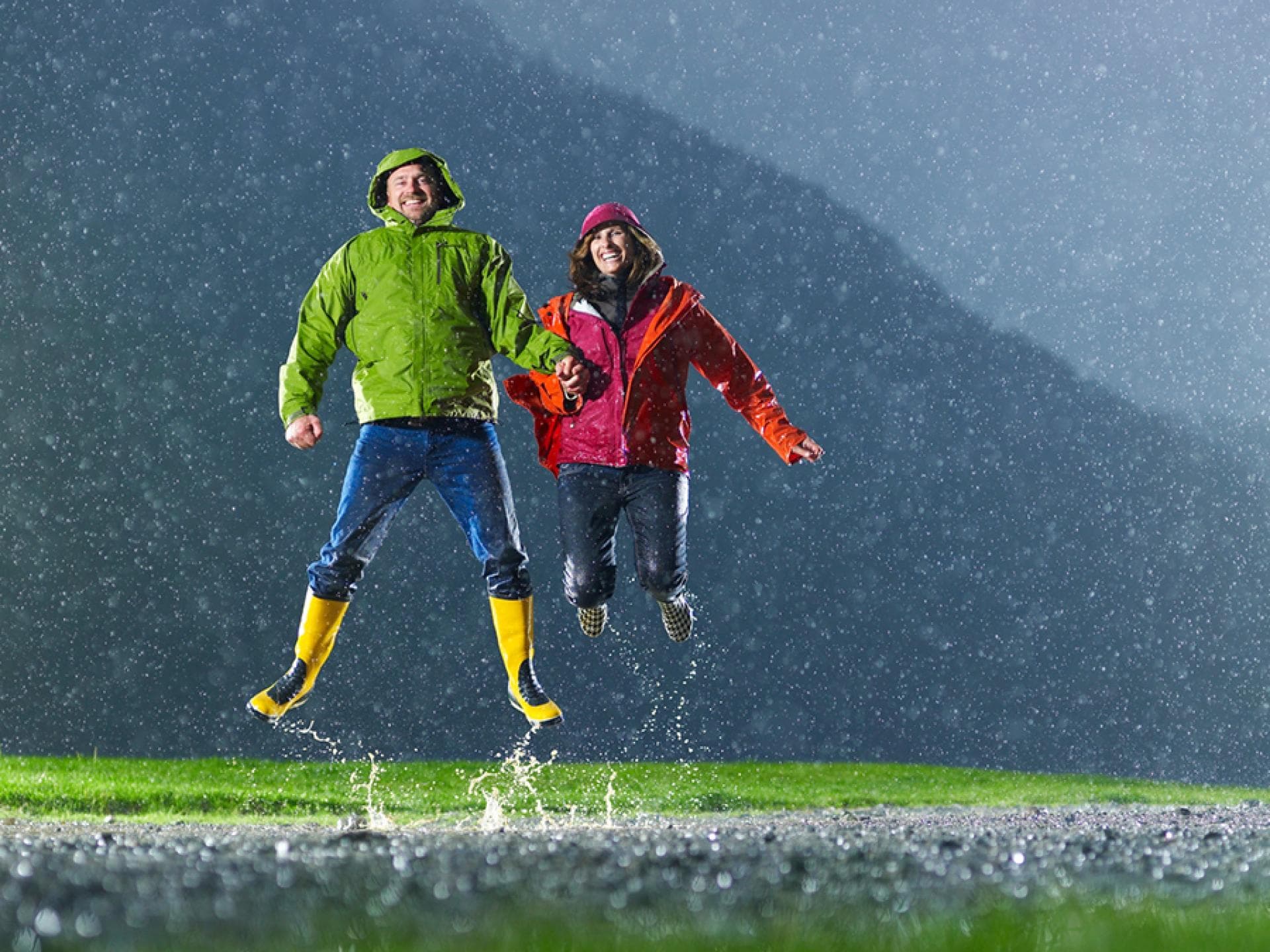 Menschen springen in einer Pfütze - obwohl es regnet sind sie von Wetterfühligkeit nicht betroffen