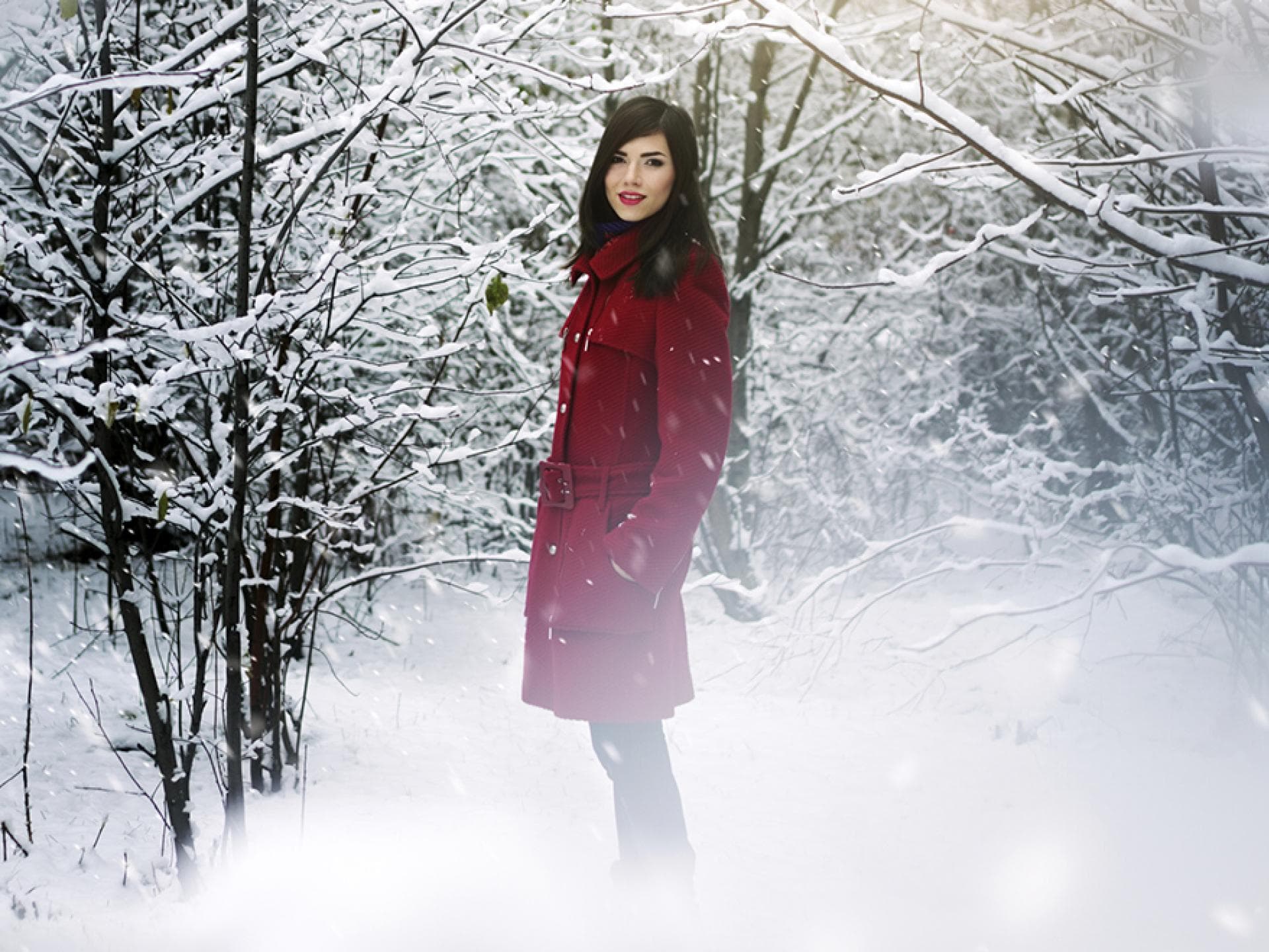 Wintermantel Frau steht im verschneiten Wald mit rotem Mantel - Tipps für das richtige Winteroutfit