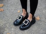 Frau trägt schwarze Loafer mit großer Schnalle.
