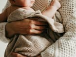Frau hält ein Baby, das in eine Decke gehüllt ist.