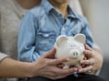 Sparschwein in der Hand von einer Frau mit einem Kind auf dem Schoß