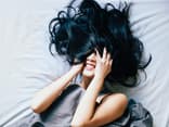 Frau liegt im Bett und hat ihre Haare im Gesicht
